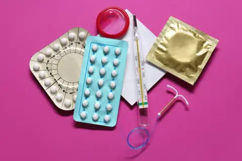 Getty Images Photo of a range of contraception spread out on a table, including the pill, contraceptive coil and a condom in a wrapper, on a bright pink background