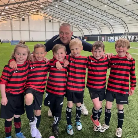 Supplied A group of children in red and black football tops and boots, a coach is in the background