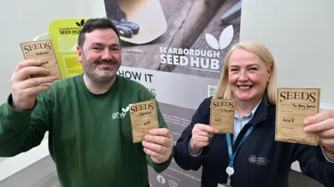 Darren Mancrief, founder and co-chairman of GROW Scarborough, with Scarborough library supervisor, Deirdre Antonescu. They hold up packets of seeds.