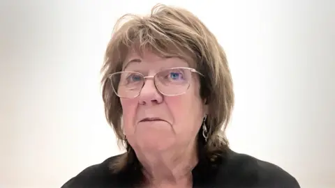 Scottish Parliament A woman with light-coloured hair looks at the camera during a video call. She is wearing a black top and glasses. 