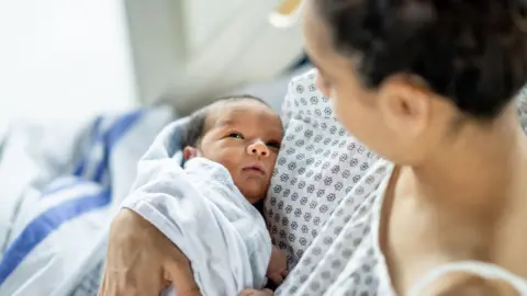 A woman cradles her newborn baby in her arms, wearing a hospital gown