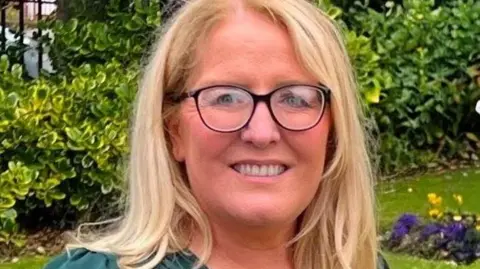 Ciara McKay has long blonde hair and is wearing a green dress.
She is standing in a large field with a number of green bushes in the background.