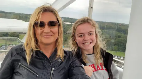 Laura Summers Maisie Summers-Newton and her mother Laura pose in a cable car. Laura is a blonde haired woman and wears sunglasses and a black leather jacket. Maisie is also blonde, and wear a grey sweatshirt and black gilet. 