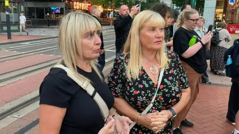 Two blonde women with others in the background.