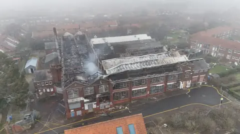 Shaun Whitmore/BBC Smoke coming off of the derelict factory which was on fire. It is a large building with hundreds of window pains. The picture is taken from above.