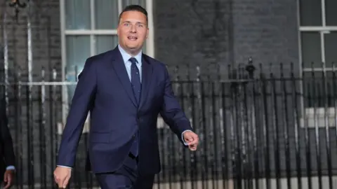 Getty Images Wes Streeting wearing a navy blue suit and tie walks past the railings outside Downing Street. He is photographed mid-stride, with government buildings and tall windows visible in the background.