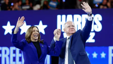 Vice President Kamala Harris and Tim Walz holding hands and waving astatine  the DNC