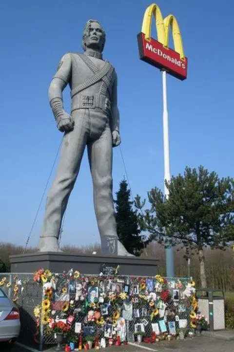 Peter Van Gelder A Michael Jackson statue, stood near a McDonald's golden arches sign, surrounded by a small fence covered in flowers, letters and other tributes.