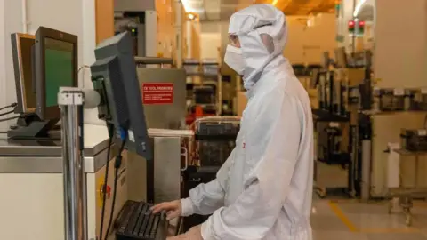 Getty Images A worker dressed in white specialised personal protective equipment uses a computer in a silicon semiconductor manufacturing plan owned by Nexperia in the UK.