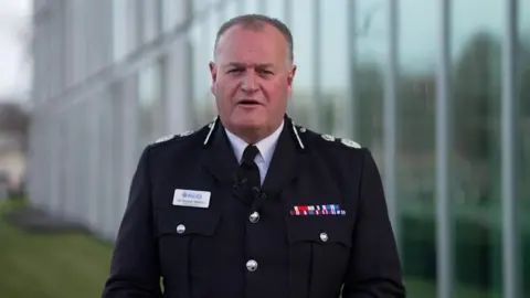Greater Manchester's chief constable Sir Stephen Watson is wearing his dress uniform and speaking directly to the camera.