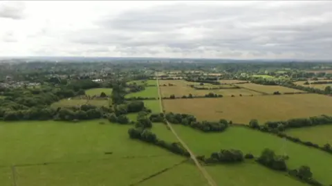 An aerial showing green fields in Oxfordshire, with a road running up the centre of the picture.