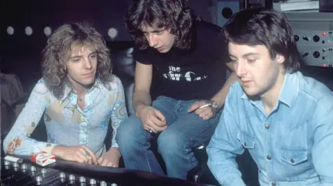 Chris Kimsey Musician Peter Frampton and producers Bob Mayo and Chris Kimsey are hunched over a mixing desk at NYC Electric Ladyland Studios. He is wearing a light blue denim shirt.