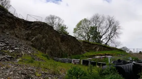 Lock's Hill in Kingsbridge, Devon, with construction materials at the bottom of a slope and fencing at the top of it