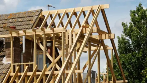 A wooden roof structure being built on to the side of a existing house