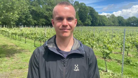 Marcella Whittingdale/BBC A man wearing a black light jacket and is standing at a vineyard.