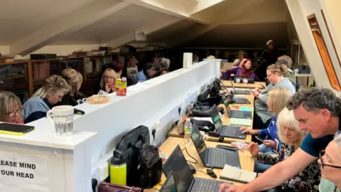 Women sit around two long desks, with laptops open in front of them.