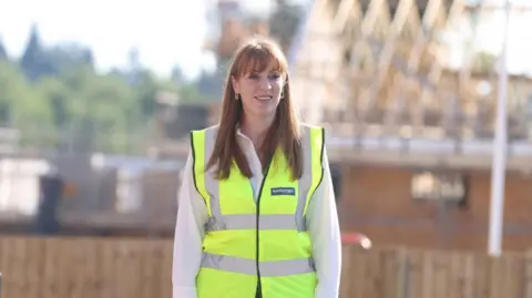 Reuters Deputy Prime Minister Angela Rayner visits a housing development site in Basingstoke while wearing a white shirt and a yellow hi vis jacket