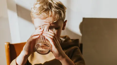 A boy with blond hair drinking from a glass of water