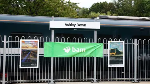 GWR A train platform with a sign which reads 'Ashley Down' and a green Great Western Railway train on the track