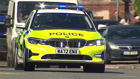 A police car on blue lights driving between traffic on a road. 
