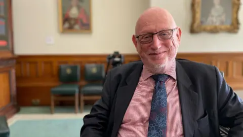 Chief Commissioner Max Caller in a red and white striped shirt and blue floral-print tie.