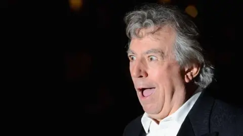 Getty Images Terry Jones looking amazed, wearing a white short and black jacket.