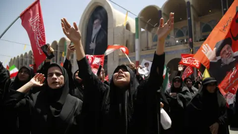 Getty Images Iranians gather to grieve, with one woman crying up to the sky with her arms stretched up