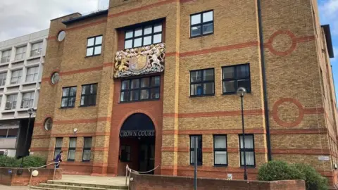 Brain Farmer/BBC The outside of St Albans Court Court, showing a brick building, with a courts of justice coat of arms. with black windows, a large entrance and steps up to the building. 