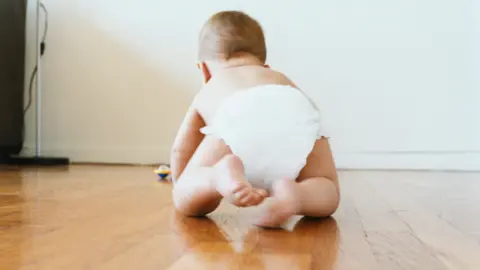 A baby crawling on a wooden floor