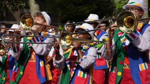 PA Media A band of trombone players in colourful uniforms at the Children's Day parade