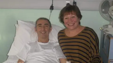 Steve Cervi Steve Cervi, in his 50s, on a hospital bed, wearing a white hospital gown, propped up on a white pillow. He is smiling at the camera next to a woman, also smiling broadly, with short brown hair and a brown and blue striped top.