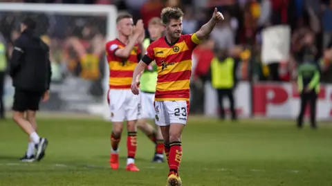 Two Partick Thistle fans in red and yellow hooped shirts salute fans after a game