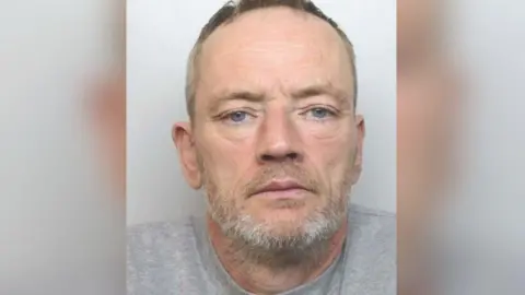 Mugshot of Paul Rowlands. He is wearing a grey shirt and has a grey beard.