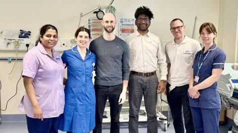 Sheffield Teaching Hospitals NHS Foundation Trust Three women and three men stand smiling in a hospital ward. The women are wearing nurse uniforms.