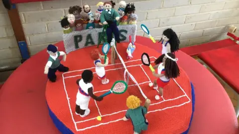 The Secret Society of Hertford Crafters Knitted tennis players play in front of a crowd of spectators, with 'Paris' written in the stand