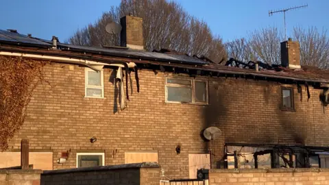 Luke Deal/BBC Three conjoined homes have been affected by the fire. The roof - in parts - is either missing or hanging off. The brickwork has been burned and some windows and doors have been boarded up.