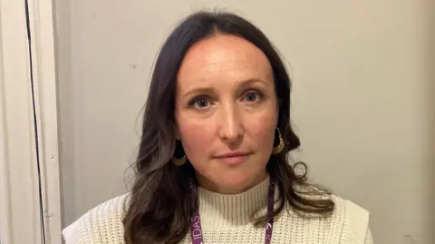 Fiona Callow/BBC Carmel Offord, who has dark hair and blue eyes. She is wearing a purple IDAS lanyard and a cream jumper.