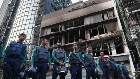 LightRocket via Getty Images Police stand in front of the daily Prothom Alo building in Dhaka's Karwan Bazar after it was attacked, vandalised, and set on fire. 