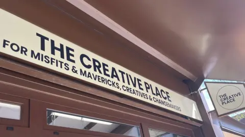 Isabella Verona/BBC A close up of the shop front that reads "The creative place". Below it it reads "for misfits and mavericks, creatives and changemakers"