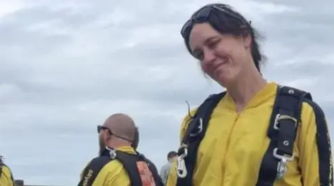 Belinda Taylor pictured wearing a bright yellow jumpsuit with black straps around her