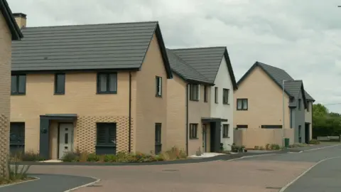 A newbuild housing estate, with four two-storey brick buildings in view