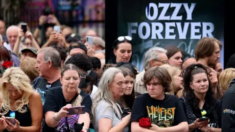 Reuters A crowd of Ozzy fans standing in front of an advertising screen showing the words "Ozzy forever"