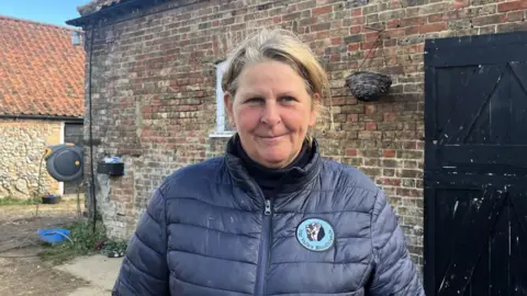 Maddy Jennings/BBC Justine Ward wearing a blue coat and standing in front of what appears to be a barn