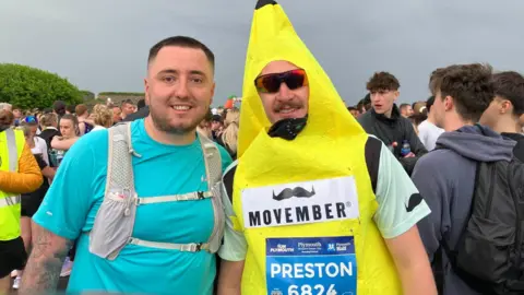 Jack Lambert (left) and Preston Wilkins (right) ready to set off for the Plymouth half marathon on the Hoe. Preston is wearing a banana fancy dress costume and sunglasses. Jack is wearing a blue t-shirt.