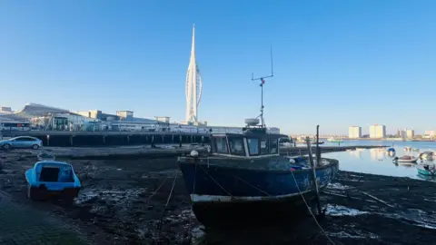 tonyswinton Small boats are on the muddy shore. The Spinnaker Tower is in the distance. 
