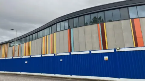 An exterior wall with bands of different colours, including yellow, orange, and burgundy.