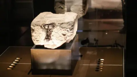 The Stone of Destiny sits on a raised platform and is lit by surrounding lights. It is concealed behind a glass case.