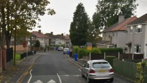 Google Google street view of semi-detached two storey houses lining a road with parked cars and trees.