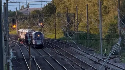 Steve Hubbard/BBC Two purple trains, with one carriage seemingly off the tracks