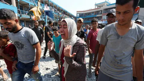 Reuters A woman reacts after an Israeli air strike on an Unrwa-run school in Nuseirat refugee camp, central Gaza, following an Israeli air strike (14 July 2024)